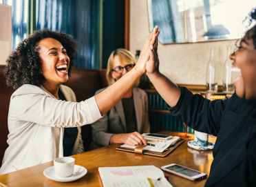 laughing women sitting in front of table doing high five clap